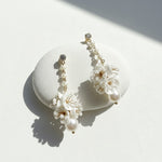 White floral drop earrings with pearl accents on textured stone.