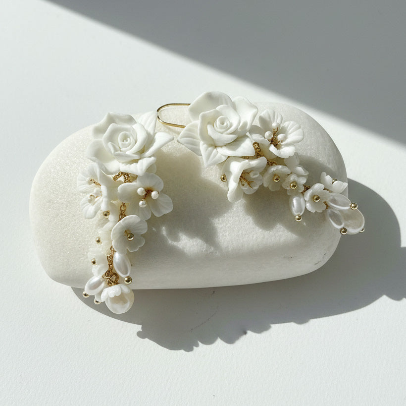 Porcelain floral and pearl drop earrings on white stone under sunlight.