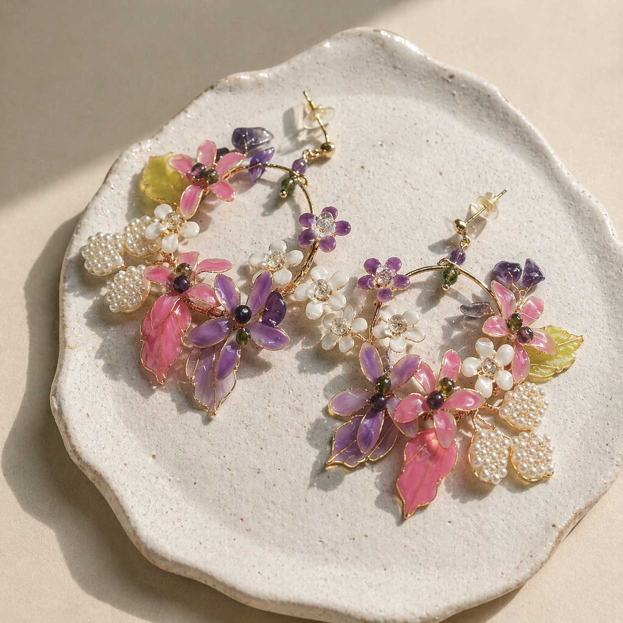 Floral earrings with pink, purple, and white flowers on a textured stone surface.
