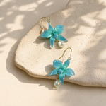 Pair of turquoise orchid-shaped earrings with pearl drops on a beige stone surface.