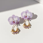 Pair of purple flower earrings with gold and pearl details on a white background