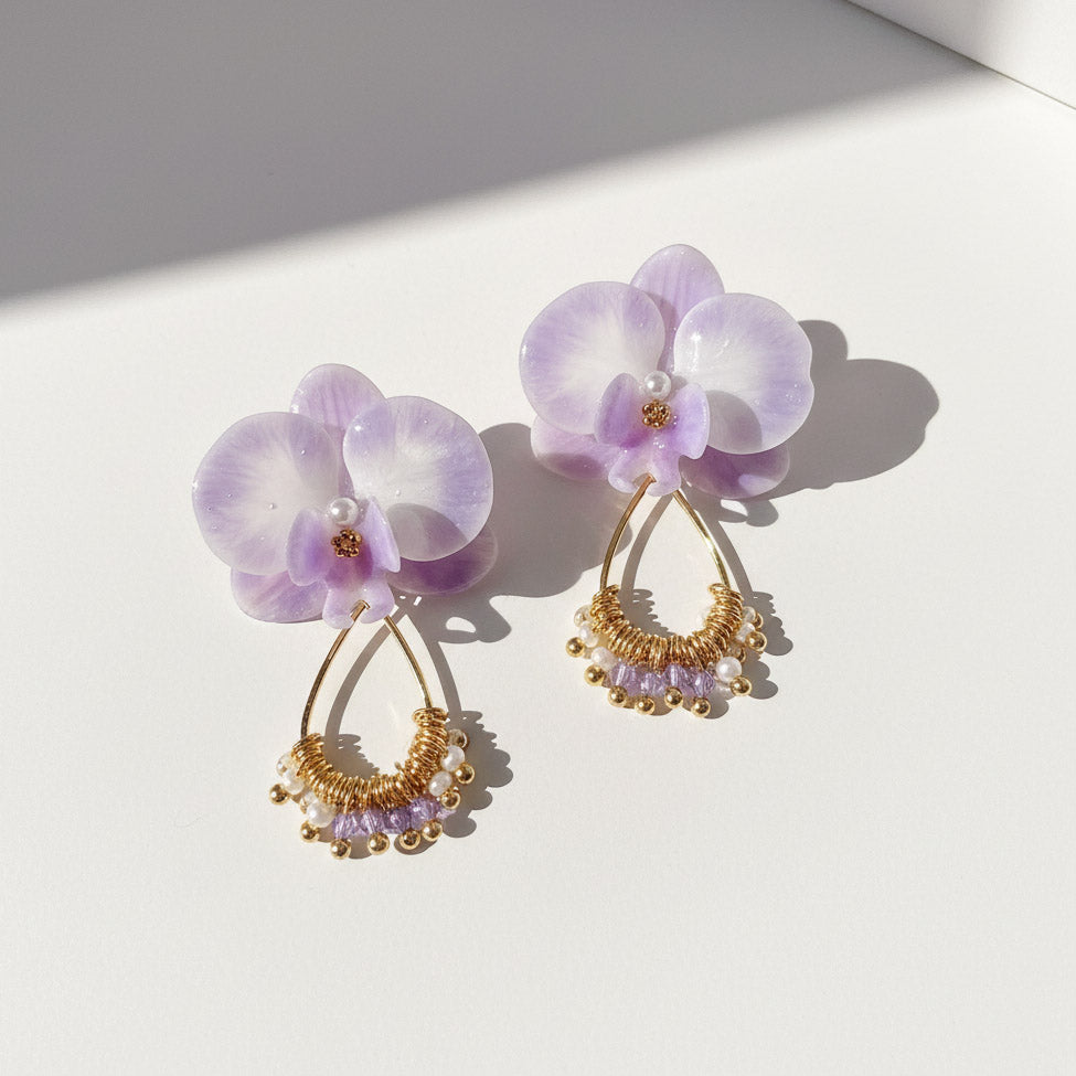 Pair of purple flower earrings with gold and pearl details on a white background