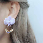 Model wearing a lavender orchid statement earring with a gold wire hoop, accented by small pearls and purple crystals.