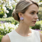 Woman wearing purple floral earrings with a blurred garden background
