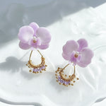 Pair of purple flower earrings with gold and beaded accents on a white surface.
