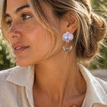 Woman wearing a purple orchid earring with a blurred natural background