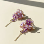 Pair of floral earrings with purple flowers and gold chains on a beige background