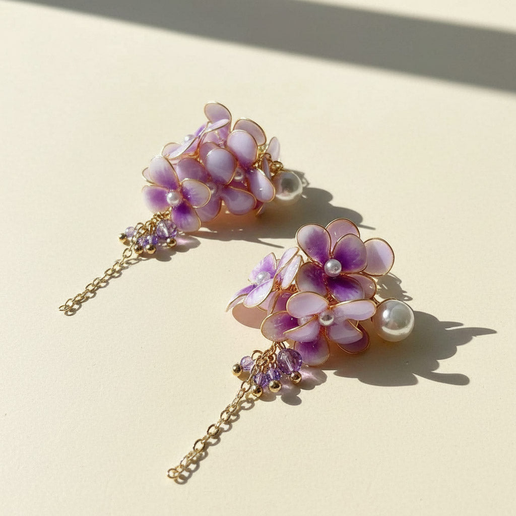 Pair of floral earrings with purple flowers and gold chains on a beige background