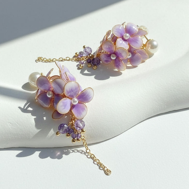 Delicate purple floral earrings with gold chains on a white surface