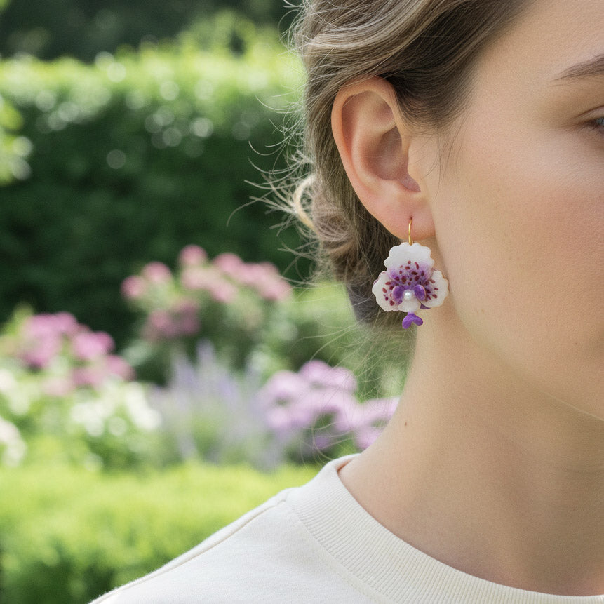 Close-up of a person wearing floral earrings with a garden background
