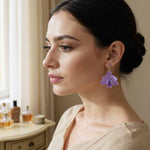 Woman wearing purple floral earrings in a softly lit room.