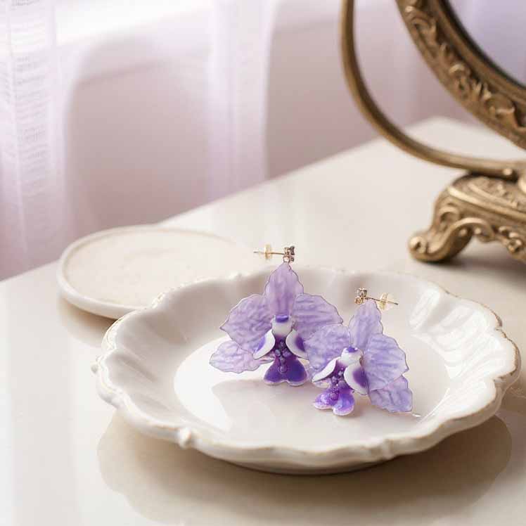 Purple orchid earrings on a white dish with a decorative mirror in the background