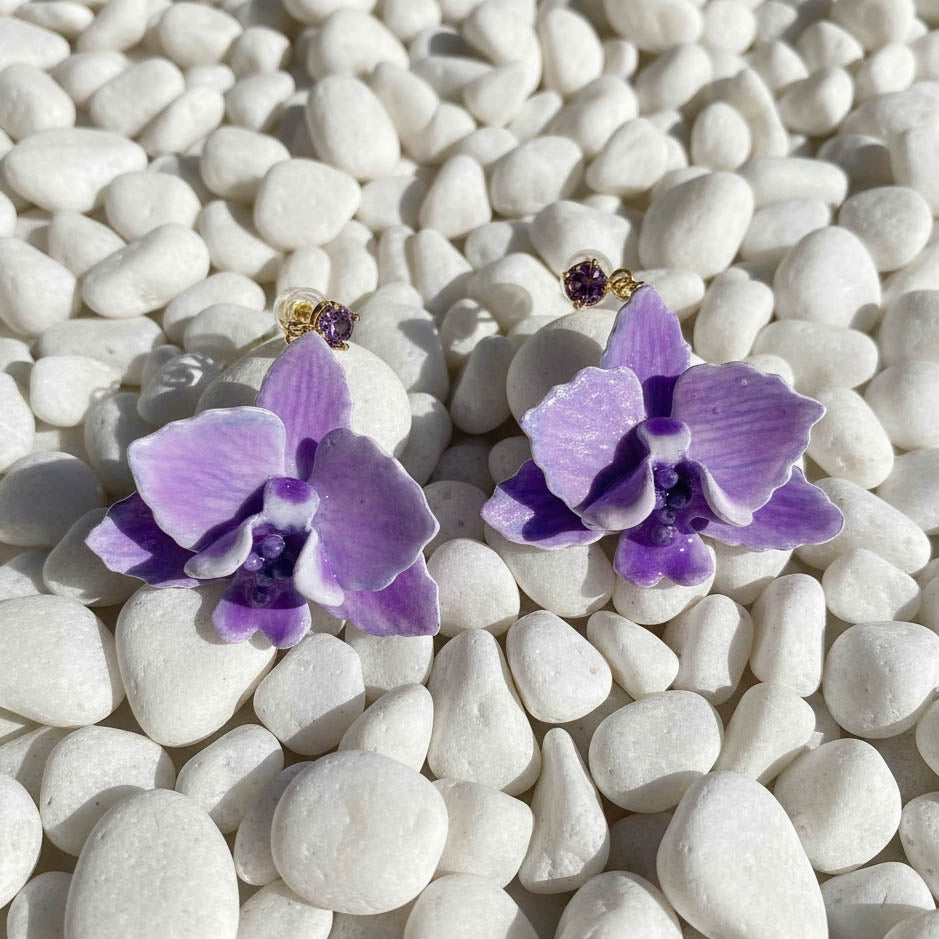 Purple orchid earrings on white pebbles