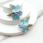 Floral  flower earrings with purple and green flowers on a white stand.