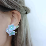 Floral earring worn by a person with light-colored hair on a plain background