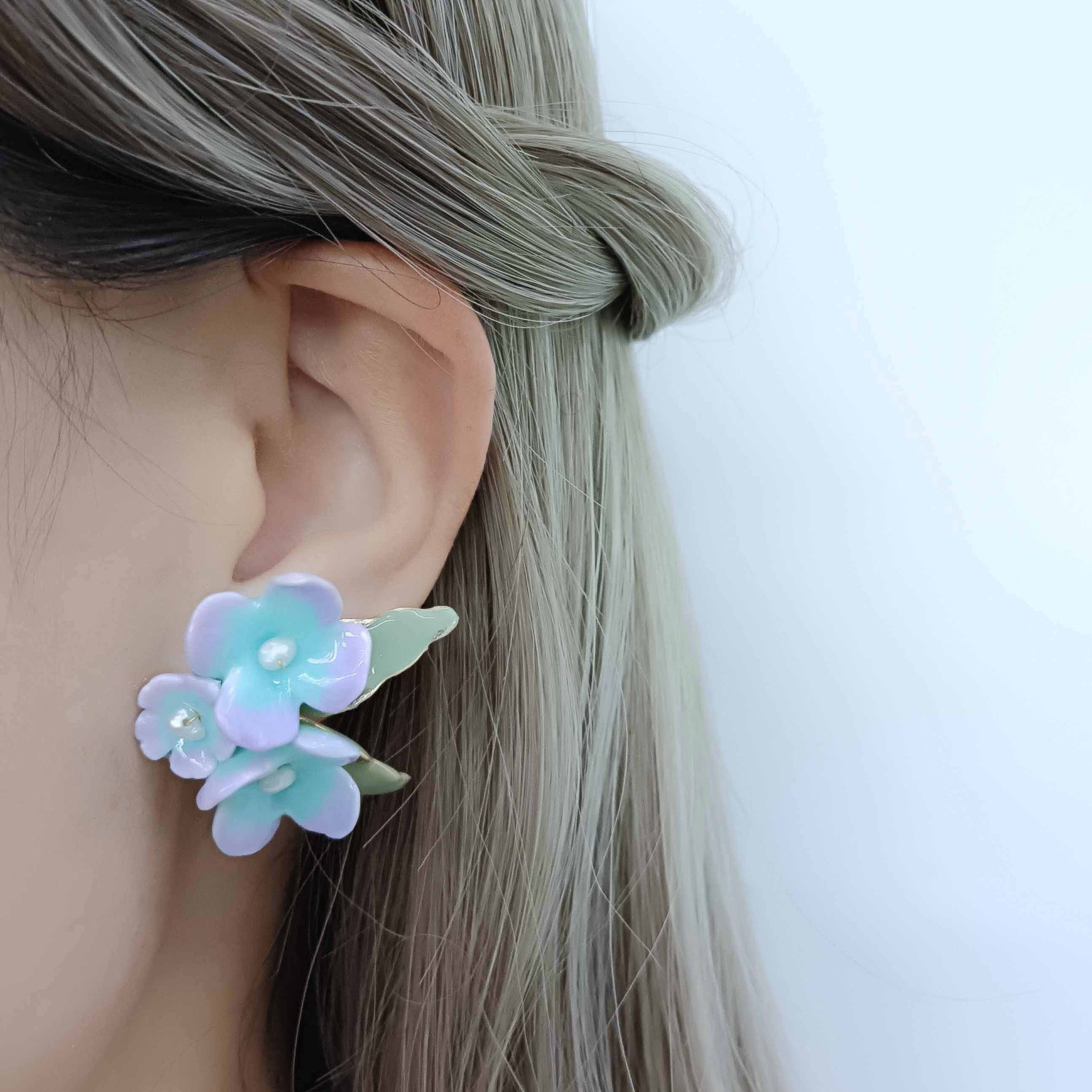Floral earring worn by a person with light-colored hair on a plain background