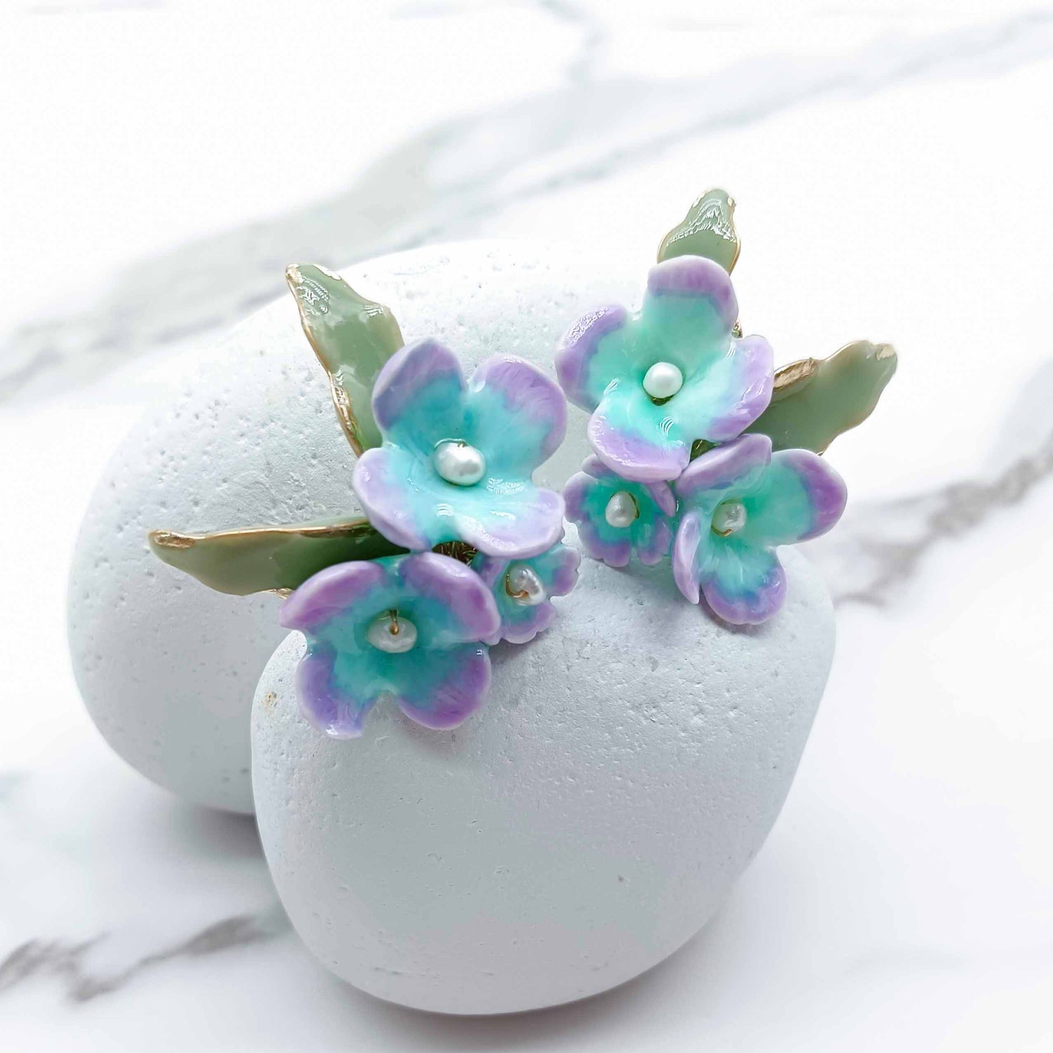 Floral earrings with purple and green flowers on a white marble surface