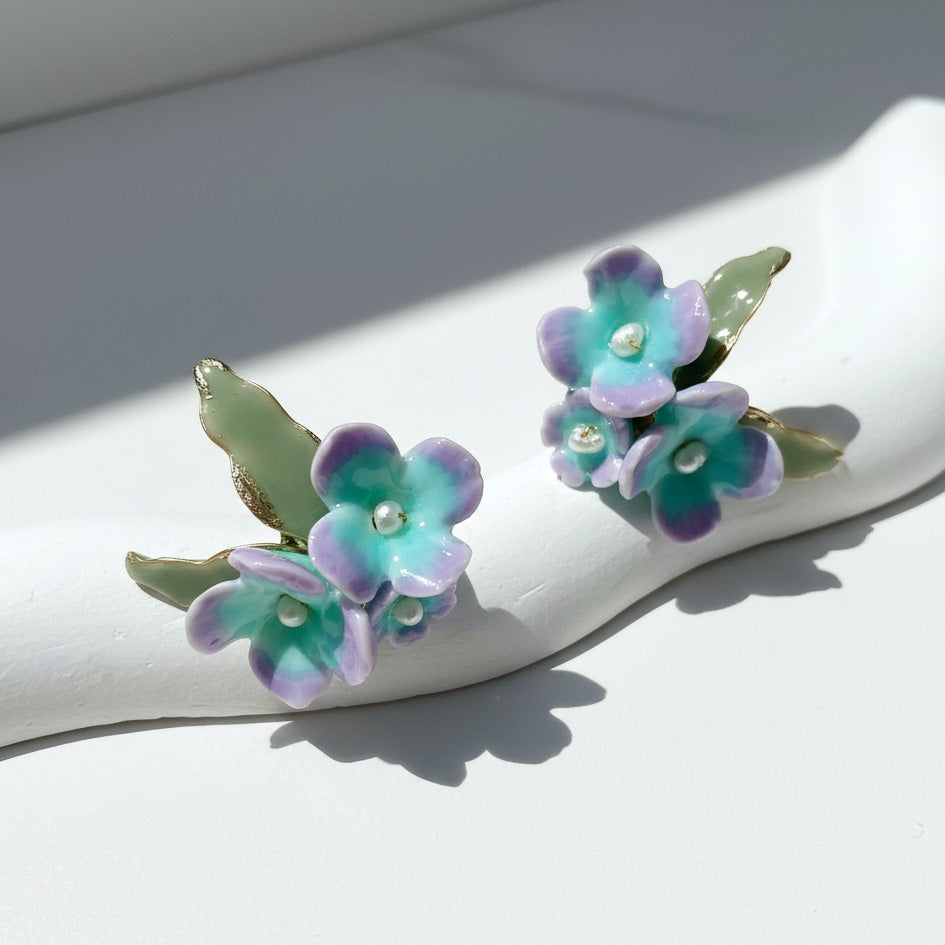 Floral earrings with purple and green flowers on a white surface