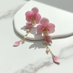 Pink flower-shaped earrings with gold chain on a white surface