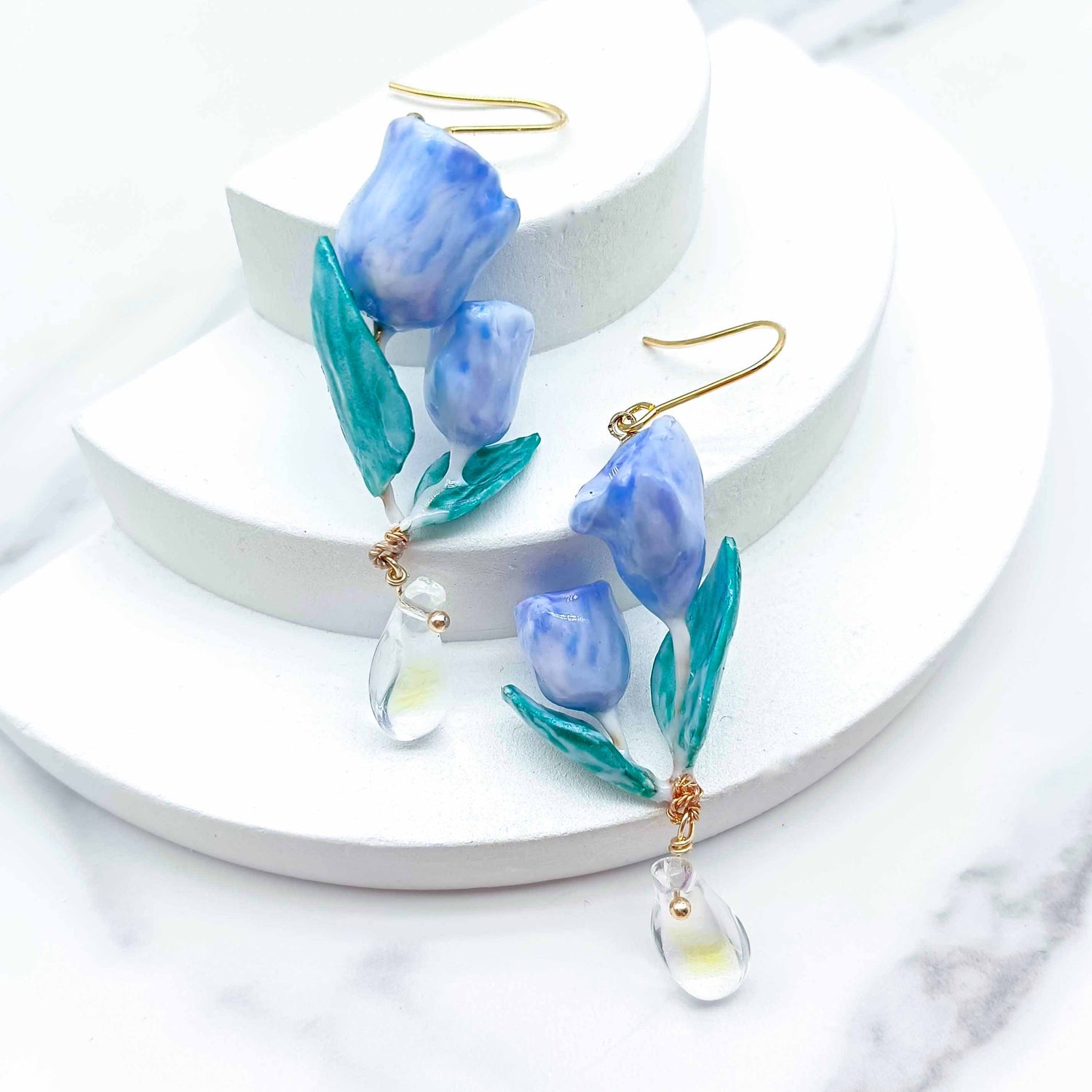 Blue floral earrings on a white circular stand with a white background