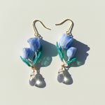 Handcrafted blue tulip earrings with green leaves and clear crystal drops, resin floral dangle jewelry on light background.