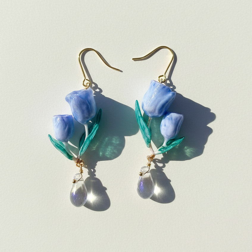 Handcrafted blue tulip earrings with green leaves and clear crystal drops, resin floral dangle jewelry on light background.
