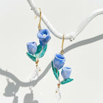 Blue tulip flower drop earrings with pearl and crystal accents, handcrafted resin floral jewelry hanging on white branch.