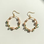 Gold hoop earrings with floral and pearl details on a light background
