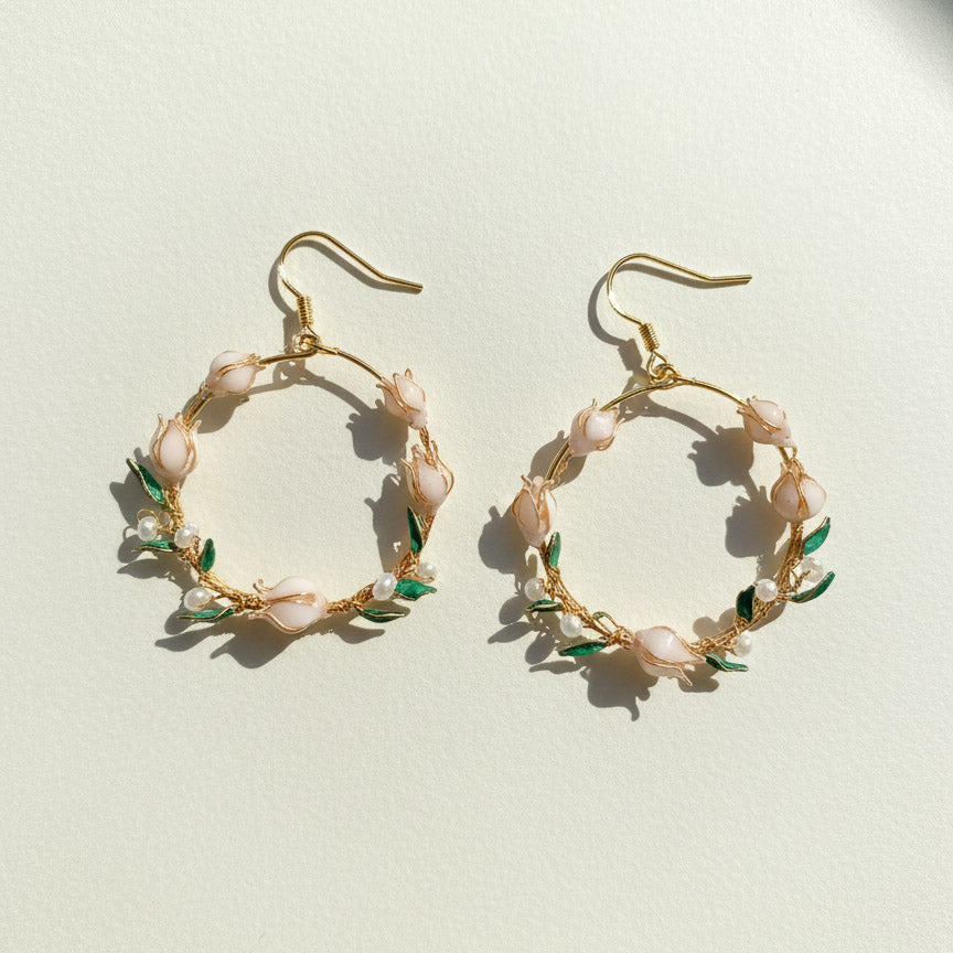Gold hoop earrings with floral and pearl details on a light background