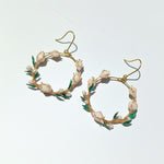 Gold hoop earrings with pearl and green leaf details on a white background
