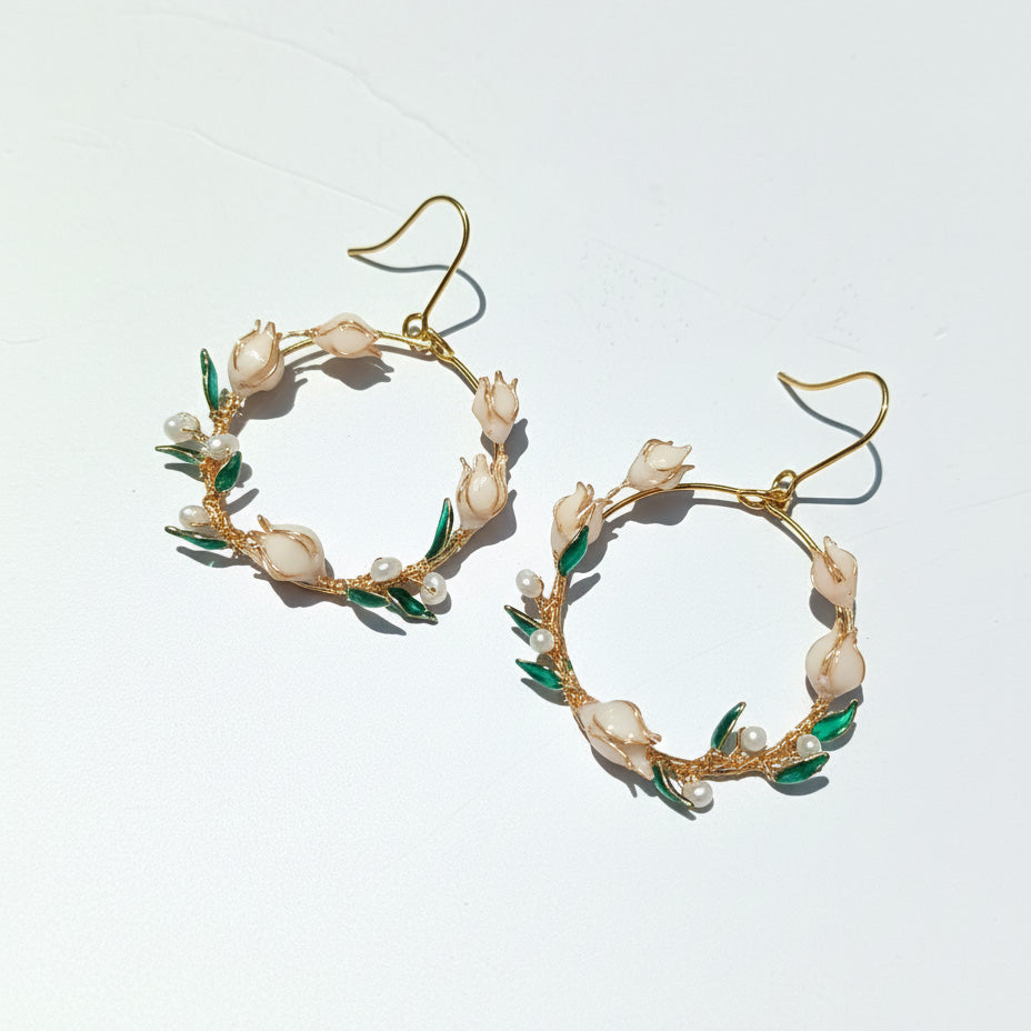 Gold hoop earrings with pearl and green leaf details on a white background