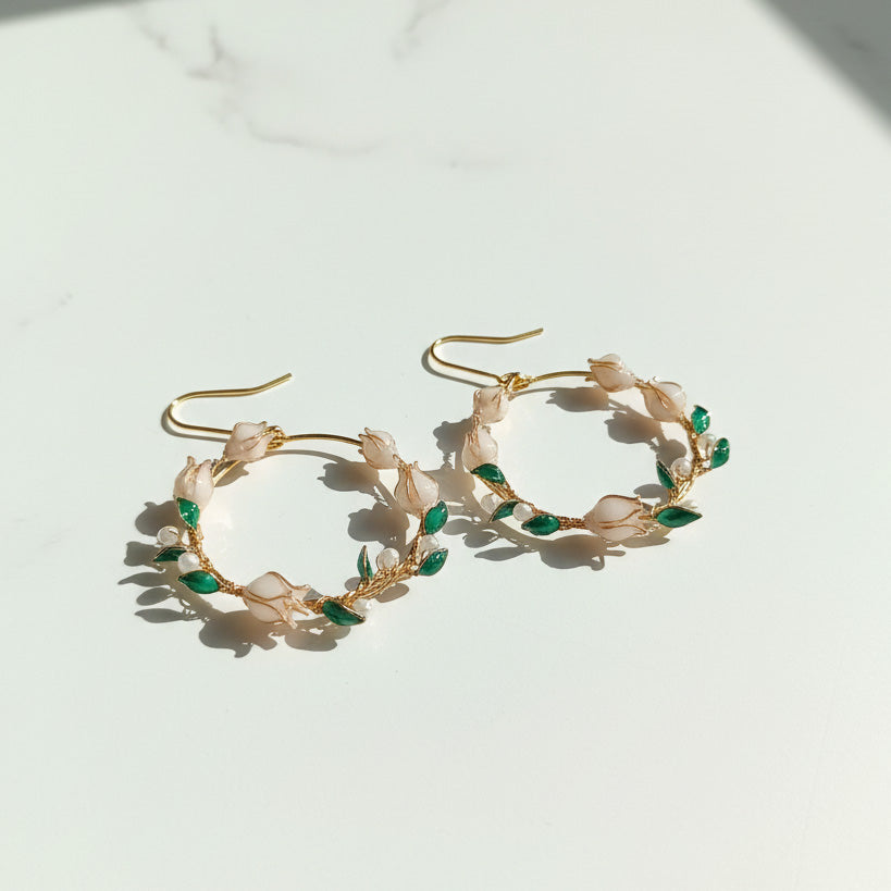 Gold hoop earrings with green leaves and pearls on a light background