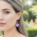 Woman wearing a purple flower earring outdoors with a blurred garden background