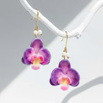 Purple orchid flower earrings with gold hooks on a white background