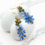Blue floral earrings with green beads on a white stone surface