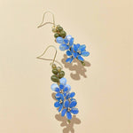 Floral earrings with blue flowers and green leaves on a beige background