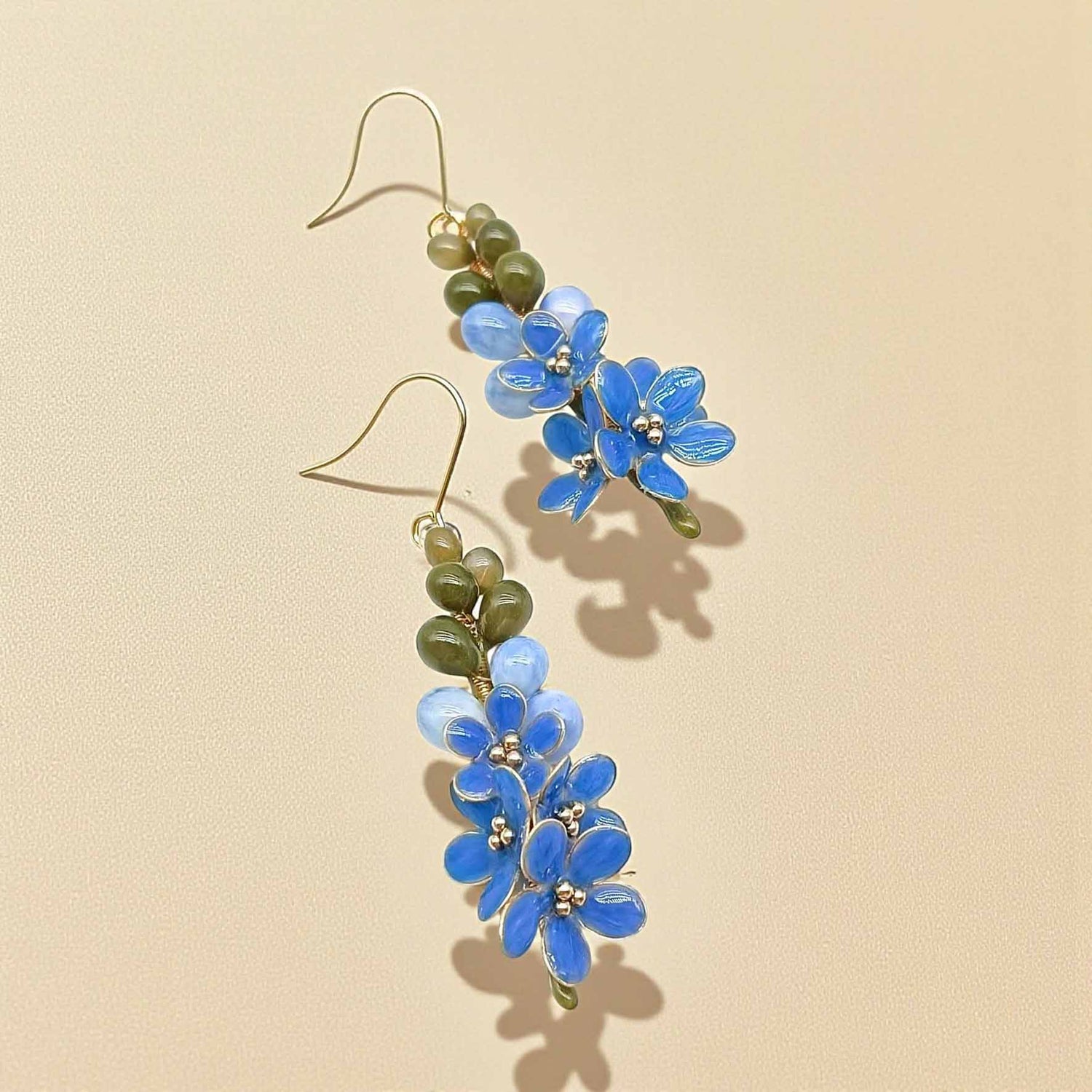 Floral earrings with blue flowers and green leaves on a beige background