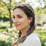 Woman with braided hair wearing purple orchid earring in a park setting
