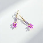 Pair of earrings with purple gemstones and floral designs on a light gray background