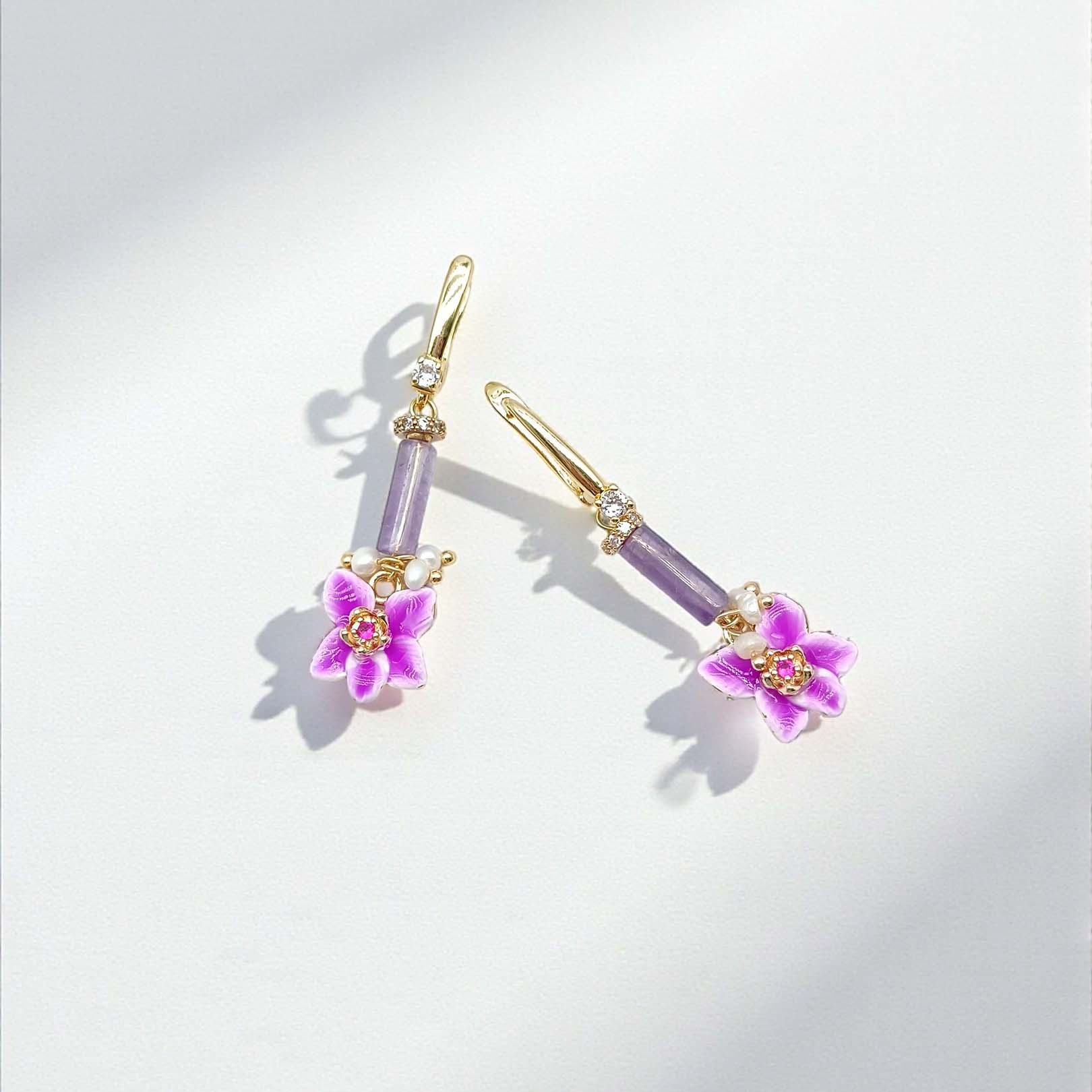 Pair of earrings with purple gemstones and floral designs on a light gray background