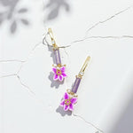 Pair of earrings with purple floral charms on a light background