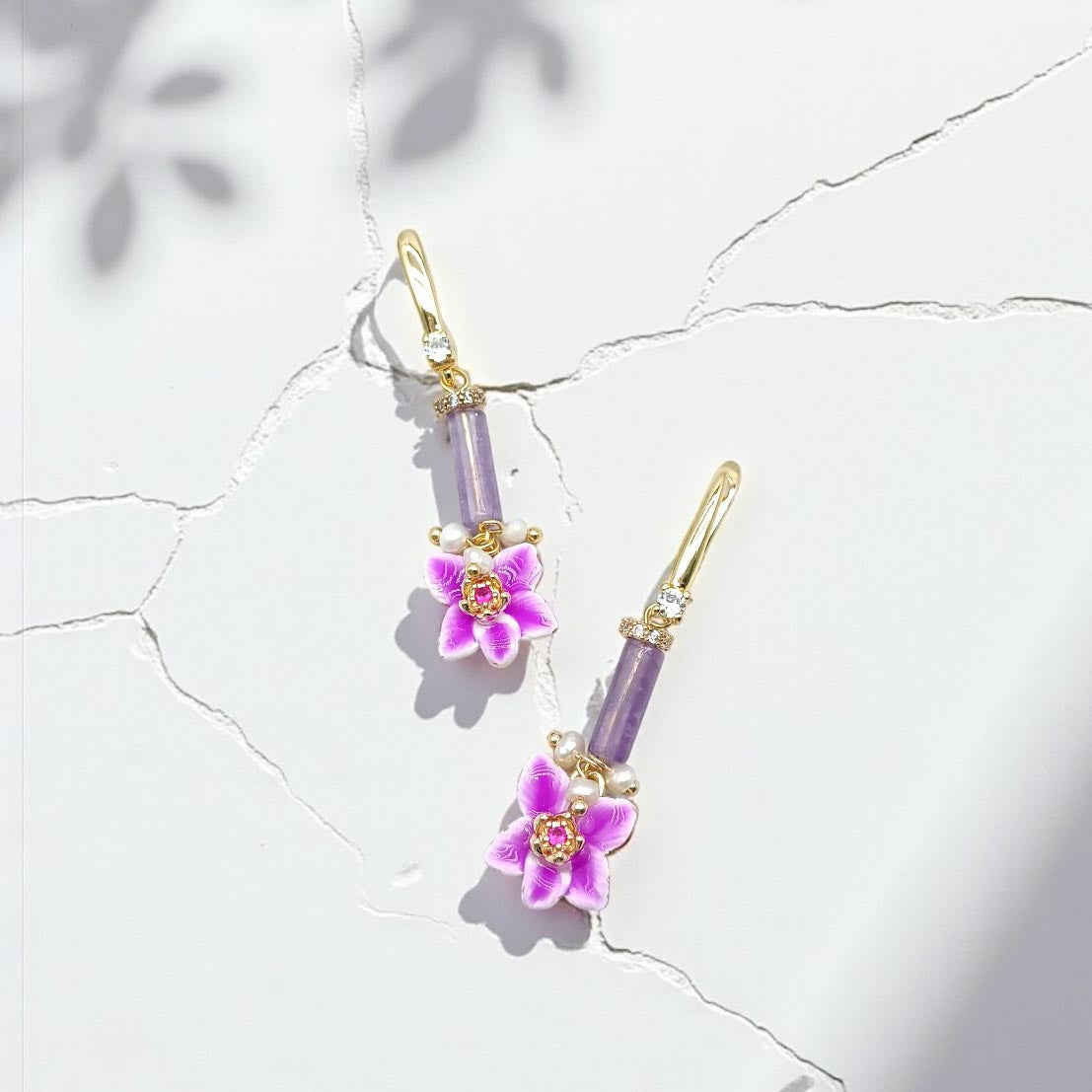 Pair of earrings with purple floral charms on a light background