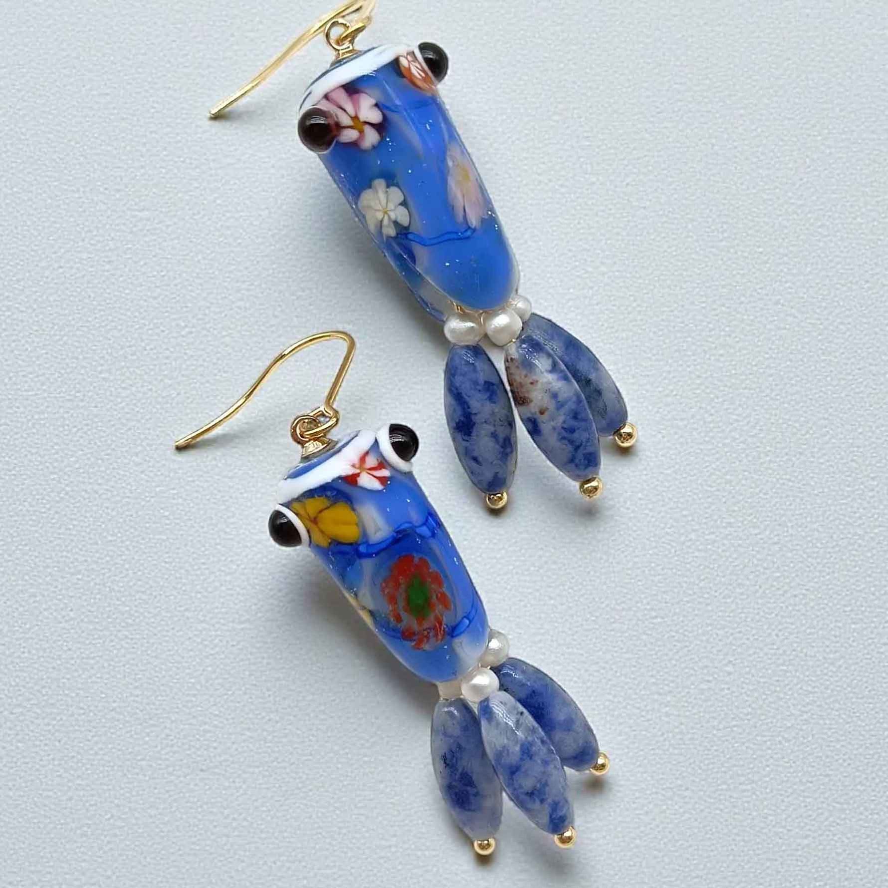 Pair of blue glass earrings with floral patterns on a light gray background
