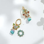 Pair of gold earrings with butterfly and floral designs on a light background