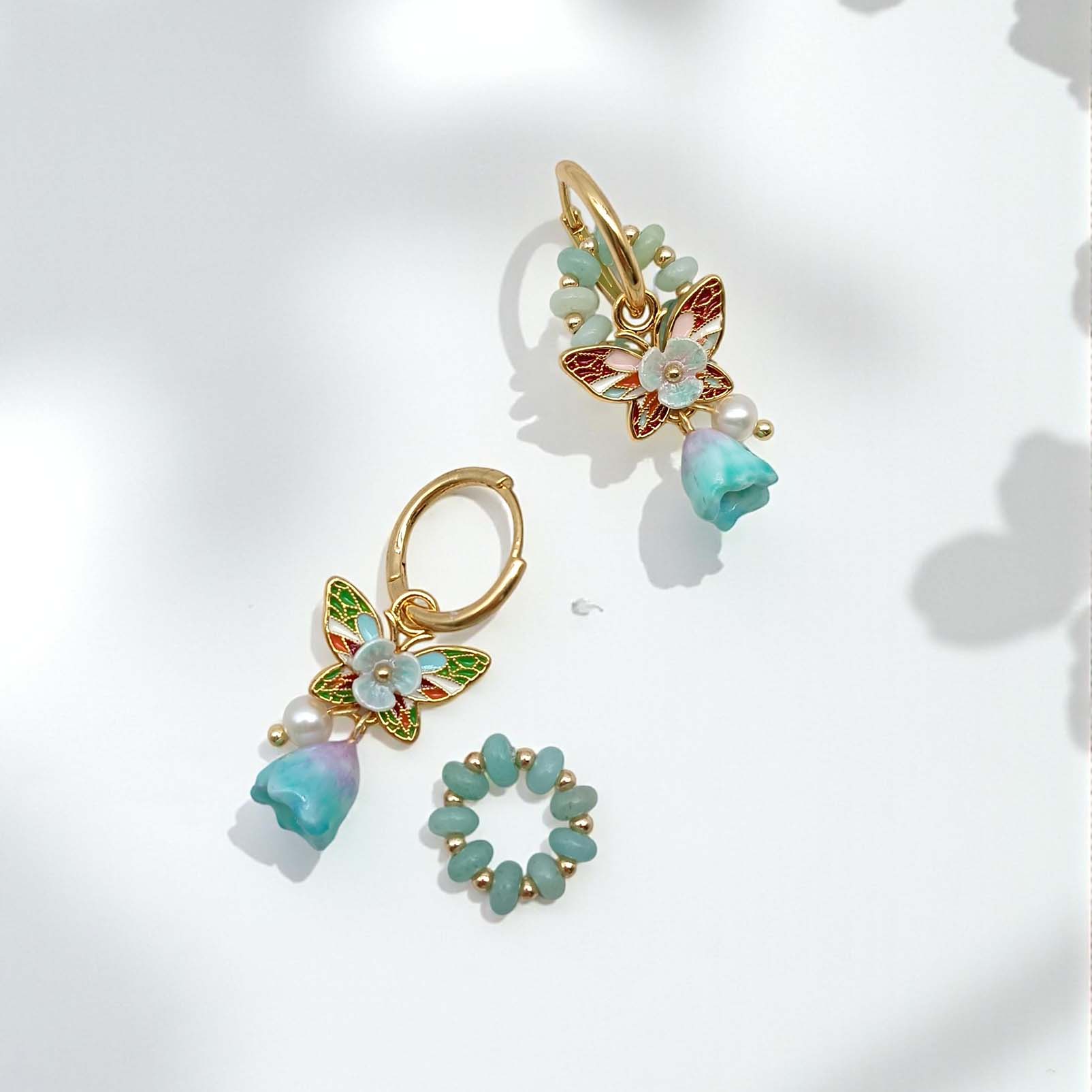 Pair of gold earrings with butterfly and floral designs on a light background