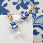 Earrings with blue and white ceramic beads and gold accents on a white surface with a blue floral pattern in the background.