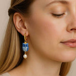 Close-up of a woman wearing an earring with a blue owl design and pearl detail.