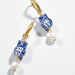 Pair of earrings with blue and white ceramic owl-shaped beads and gold accents on a light background