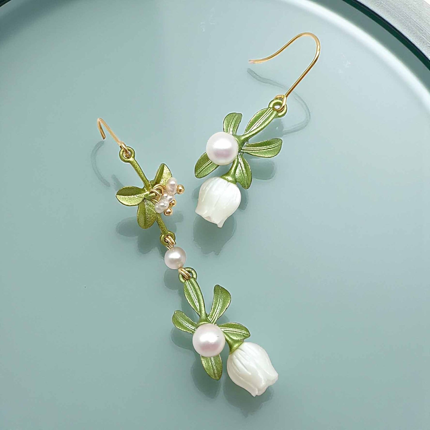 Floral earrings with green leaves and white flowers on a light blue background