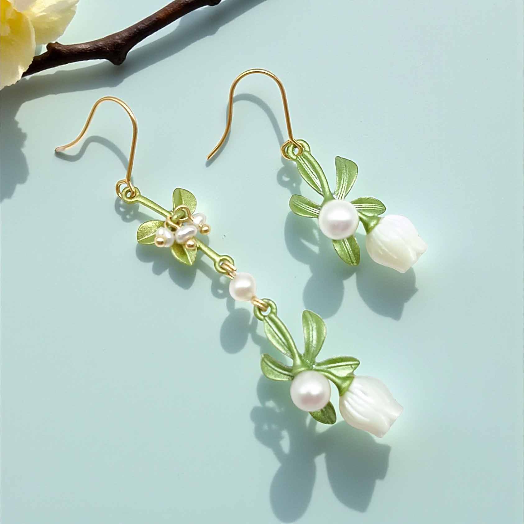 Pair of earrings with floral designs and pearls on a light blue background